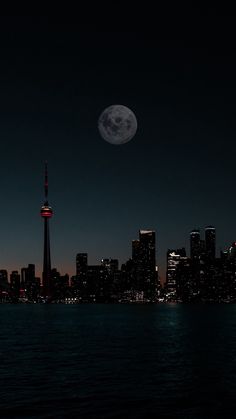 the full moon is setting over the city skyline as seen from across the water at night