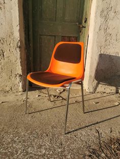 an orange chair sitting in front of a door on the side of a building next to a green door