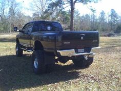 a large black truck parked on top of a grass covered field in front of trees