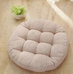 a small round cushion sitting on top of a wooden floor next to a potted plant