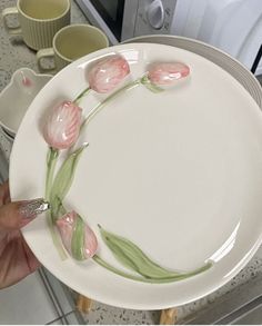 a person holding a white plate with pink flowers on it and two cups in the background