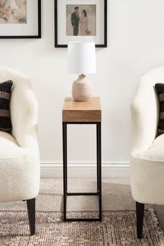 two chairs and a table with a lamp on it in front of pictures hanging on the wall