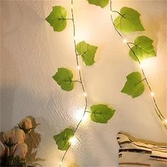 some green leaves are hanging on the wall next to a vase with flowers and lights