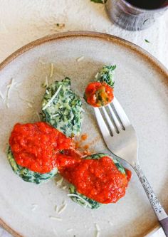 a white plate topped with spinach covered in sauce next to a fork and knife