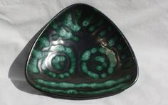 a green and silver bowl sitting on top of a white sheet