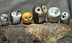 five small ceramic owls sitting on top of a tree stump with one looking at the camera