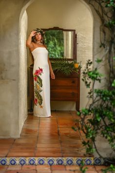 a woman in a white dress is standing by a mirror and looking at her hair