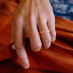 a person's hand with a gold ring on their left wrist and an orange shirt underneath