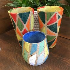 two vases sitting on top of a wooden table next to a potted plant