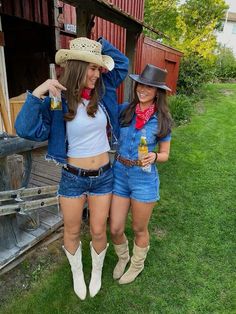 two women in cowboy hats and overalls standing next to each other on the grass