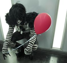 a man dressed in black and white holding a red balloon while sitting on the floor