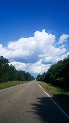 an empty road surrounded by trees under a blue sky with white clouds in the distance