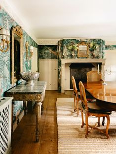 a dining room table and chairs in front of a fireplace with ornate wallpaper on the walls