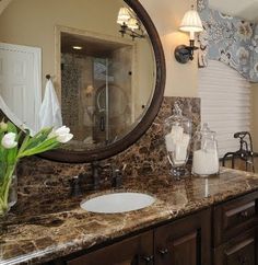 a bathroom with marble counter tops and large mirror above the sink, along with two vases filled with flowers