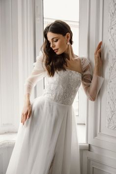 a woman in a white dress leaning against a wall with her hand on the side