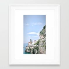 a white framed photograph with a view of the ocean and buildings on top of a cliff