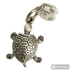 a silver turtle charm with a bell on it's back end, sitting in front of