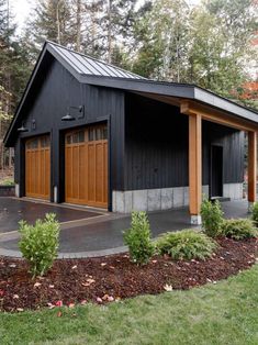 a black garage with two brown doors in front of trees and grass on the ground