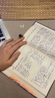 a person's hand on an open notebook next to a laptop