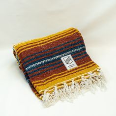 an orange, blue and yellow striped blanket with fringes on the ends sitting on a white surface