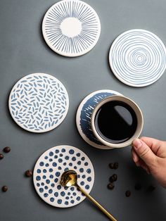 a person is holding a spoon near some plates with designs on them and coffee beans