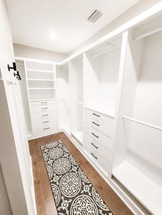 an empty walk in closet with white walls and wooden flooring, along with black and white rug