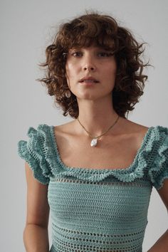 a woman with curly hair wearing a green crochet top and gold chain necklace