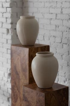 two white vases sitting on top of wooden blocks in front of a brick wall