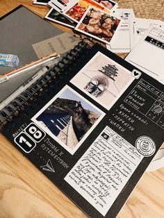 an open spiral notebook sitting on top of a wooden table next to papers and pens