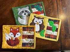 three small quilts with animals on them sitting on a wooden table next to each other