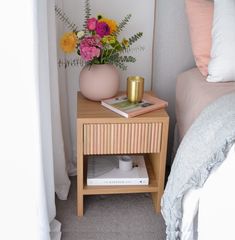 a nightstand with flowers and books on it next to a bed in a small room