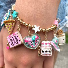 a child's hand with several charms on it and a birthday cake, ice cream cone, cupcakes, starfish, heart, donut