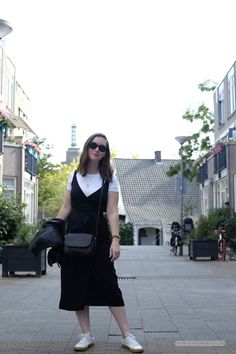 a woman is standing on the sidewalk with her hand in her pocket and wearing sunglasses