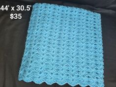 a blue crocheted blanket sitting on top of a black bed next to a pillow