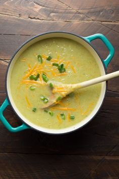 a bowl of broccoli cheese soup with a wooden spoon in it on a table