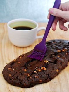 a person with a purple brush on top of a chocolate cookie next to a cup of coffee