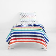 a bed with multicolored stripes and polka dots on the cover is in a white room