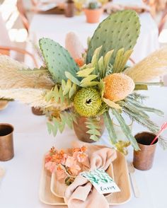 an arrangement of flowers and succulents on a table with place cards for guests