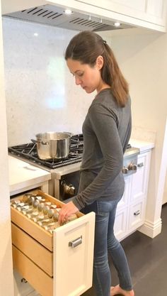 a woman standing in front of an open drawer filled with cans and pans next to a stove