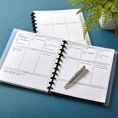 an open planner book with a pen on it next to a potted plant and fern