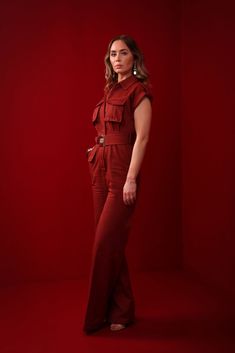 a woman standing in front of a red background wearing a maroon jumpsuit and heels