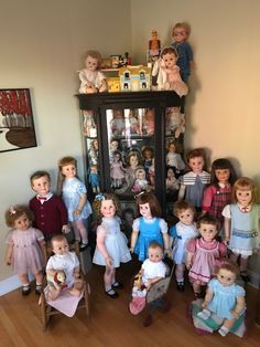 a group of dolls standing next to each other in front of a china cabinet with doll heads on top