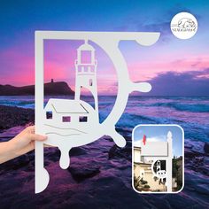 a hand holding up a cutout of a lighthouse on the beach at sunset with an ocean view in the background