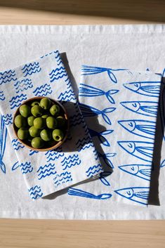 olives are in a bowl on a napkin with fish drawn on the tablecloth