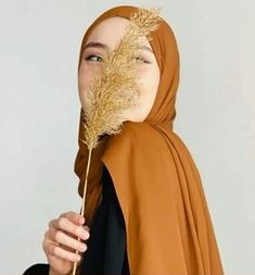 a woman wearing a brown hijab holding a dried plant