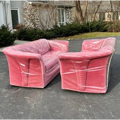 two pink couches sitting on top of a parking lot next to a house with trees in the background