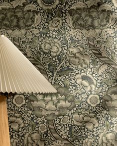 a lamp sitting on top of a wooden table next to a wallpaper covered in flowers