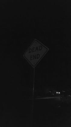 a black and white photo of a dead end sign in the dark with cars behind it