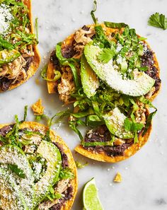 three tortillas topped with meat, cheese and green vegetables next to a lime wedge