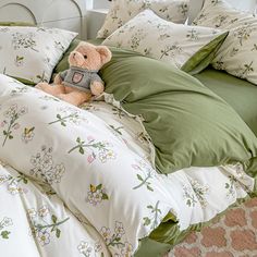 a teddy bear sitting on top of a bed covered in pillows and blankets with green comforters